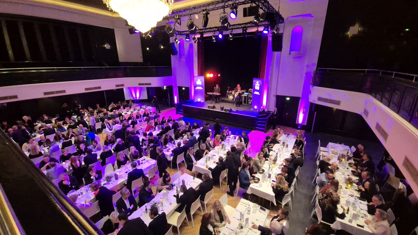 Festive ballroom with long tables, stage and purple lighting