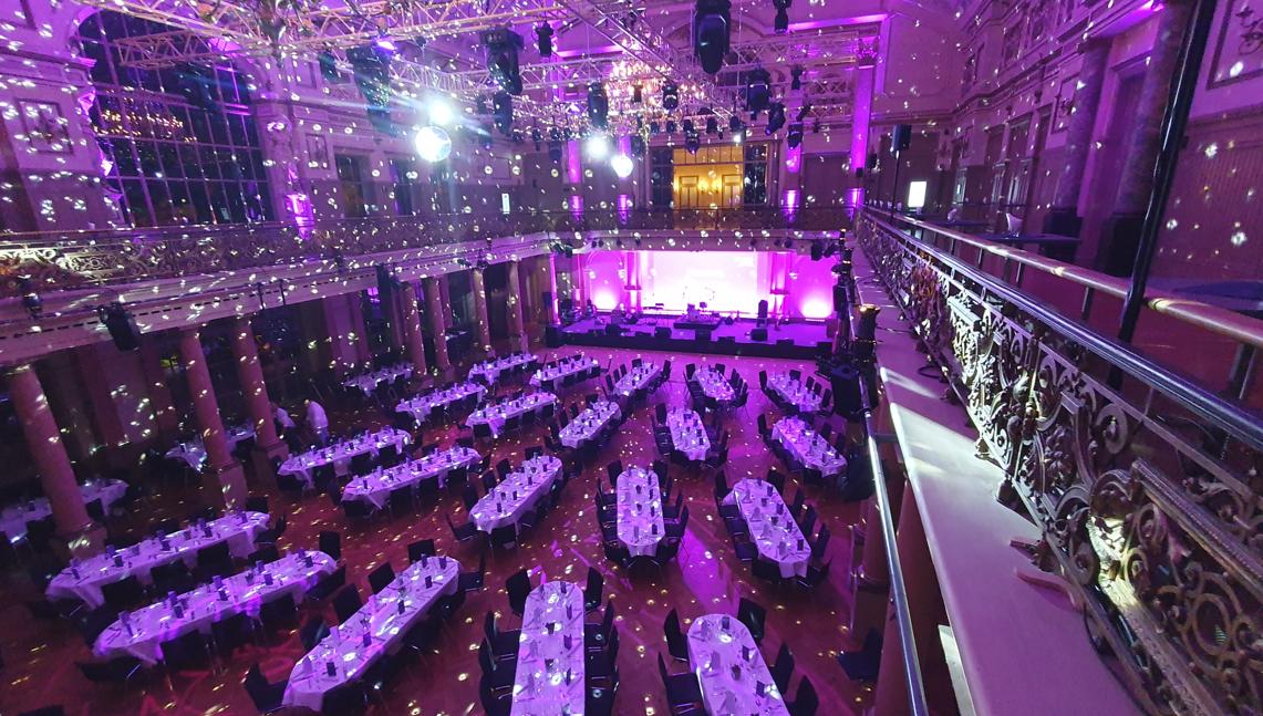 Banquet hall set for a gala dinner in violet light, with stage and gallery